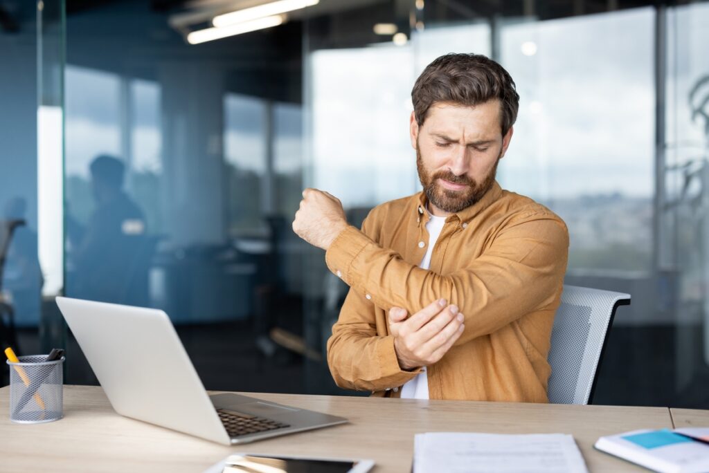 Worker experiencing elbow pain at desk illustrating pre-existing conditions workers comp claim