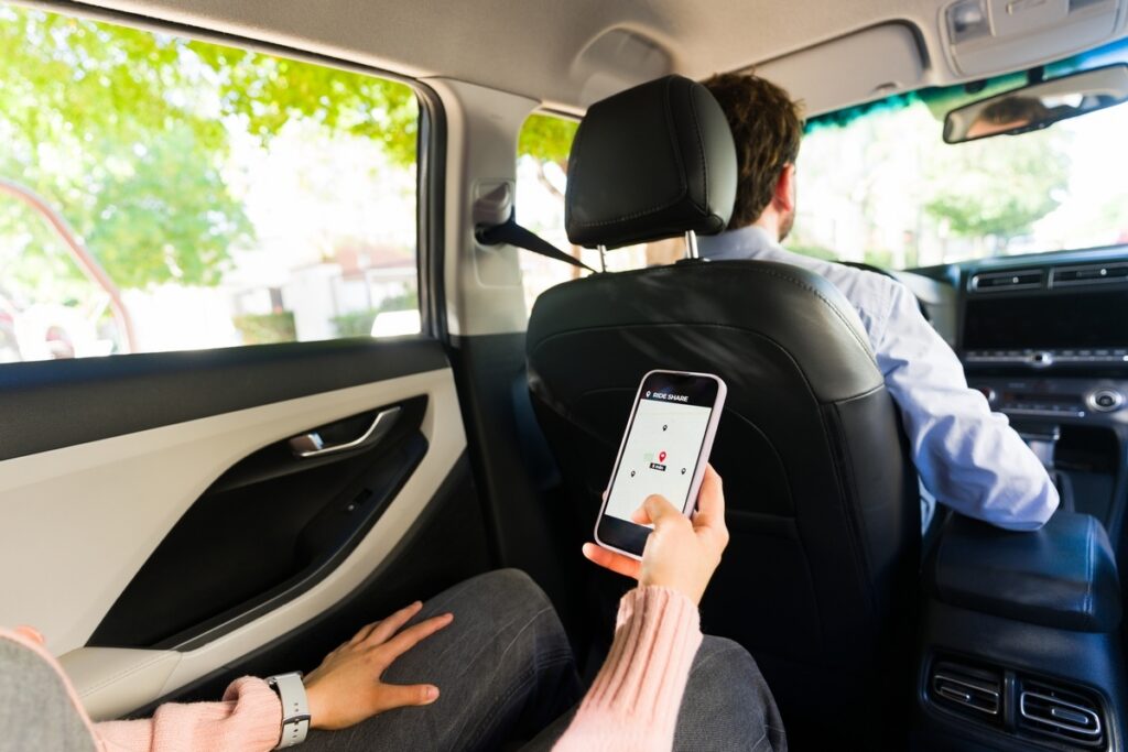 Rideshare passenger using ride share app in backseat of Uber or Lyft vehicle relevant to rideshare accident chiropractic care at Back In Motion Group Brooklyn NY